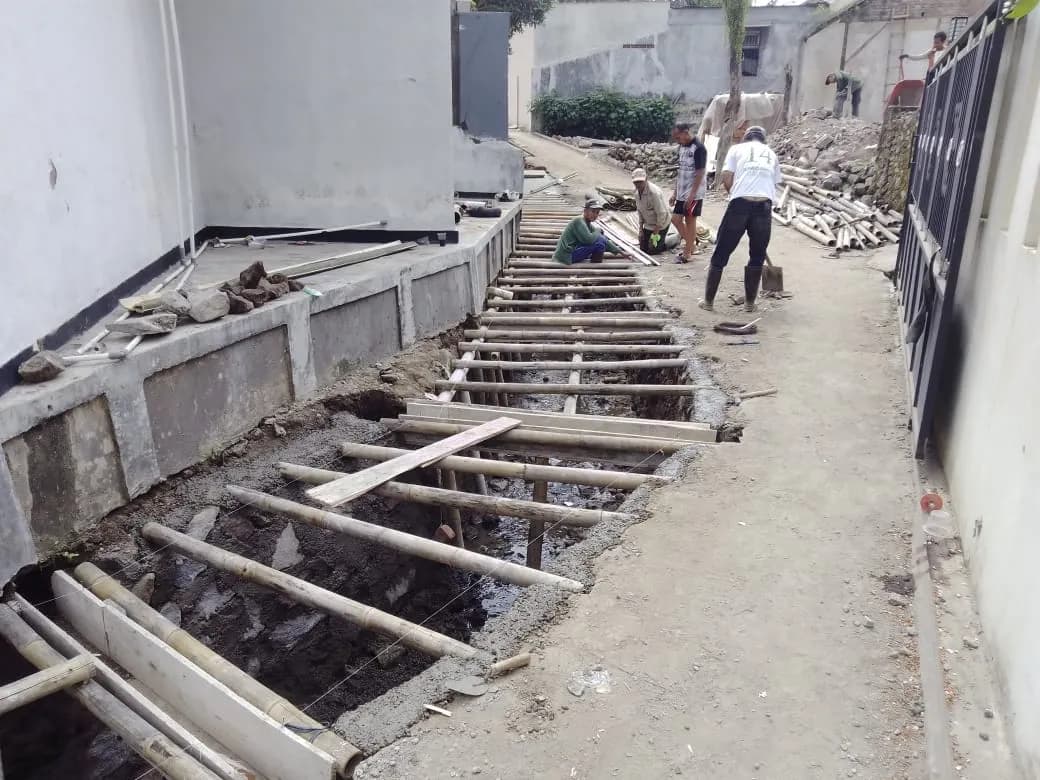 Pekerja memasang bekisting saluran beton di gang perumahan