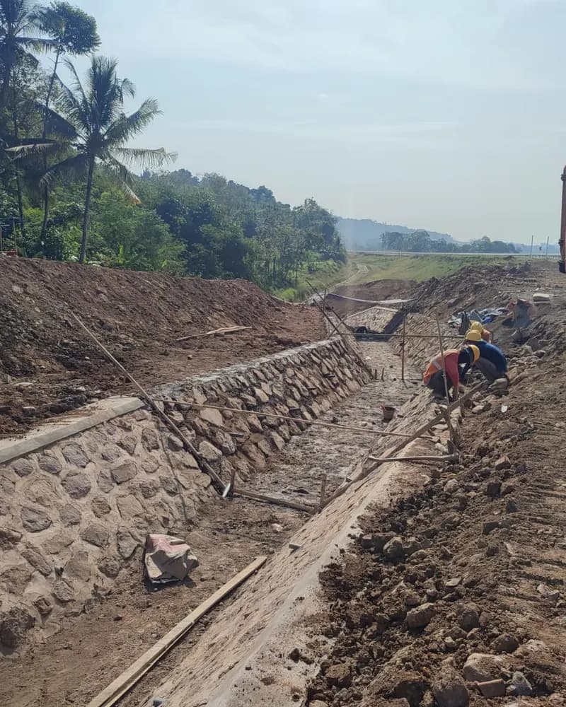 Pekerja memasang dinding pasangan batu kali di saluran